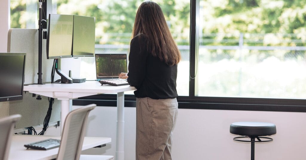 woman at standing desk working with office stool